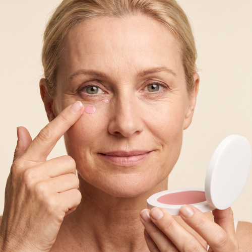 Vrouw brengt BrightLift oogcrème aan onder het oog, doosje in de hand